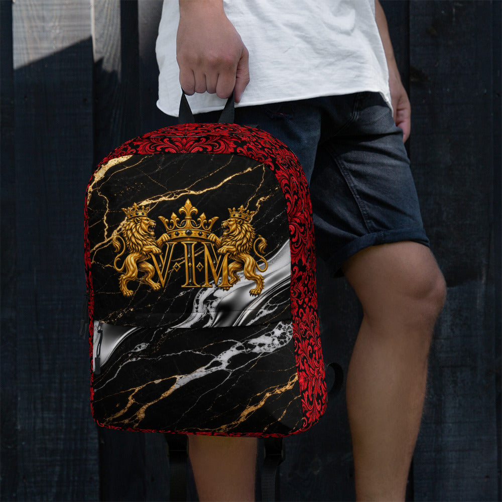 A person wearing a white t-shirt and dark denim shorts holds a custom-designed backpack. The backpack features a black marble pattern with gold veins, a red ornate patterned border, and a prominent gold crest with lions and the letters 'VIM'.