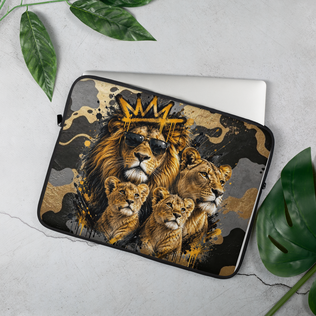 A laptop sleeve featuring a graphic print of a lion family with a crown, styled on a light gray concrete surface with green leaves.