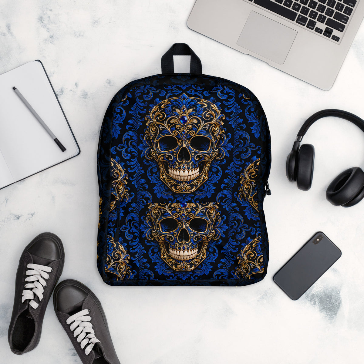 Black backpack with white design and text on a marble surface with laptop, phone, and shoes.