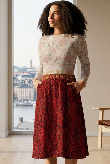 A woman modeling a two-piece outfit consisting of a long-sleeve top with a light beige and pink floral paisley pattern and a red and black damask-patterned midi skirt, paired with white sneakers, against a solid white background.