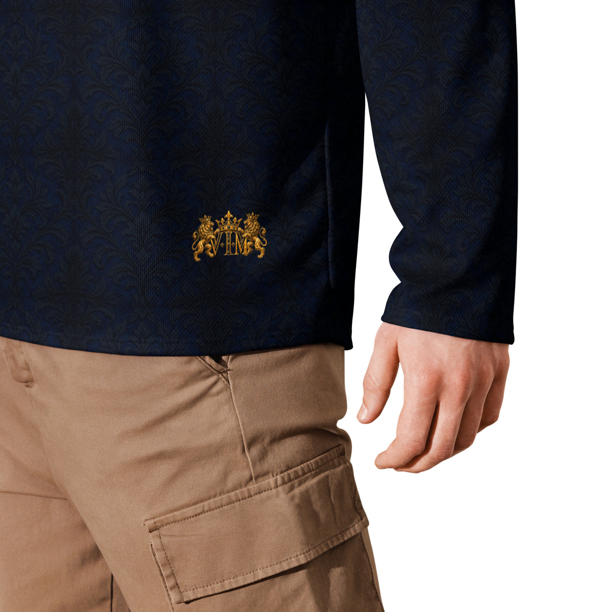 Close-up of a person wearing a dark navy long-sleeve shirt with a subtle damask pattern and a small gold crest emblem on the lower left chest, paired with tan cargo pants against a white background.