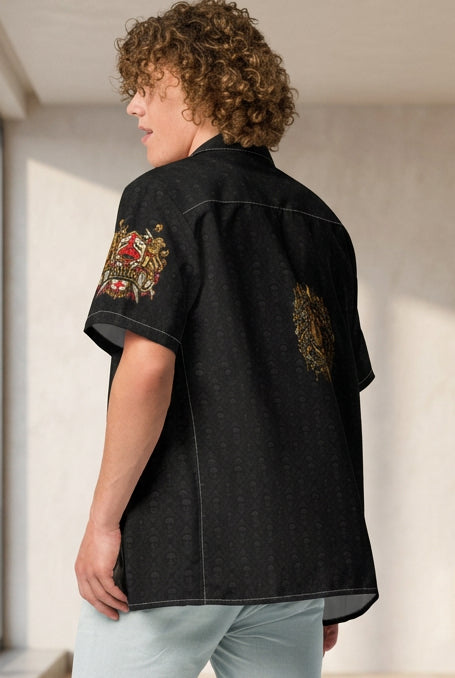 A model shown from the back wearing a black short-sleeve button-up shirt with colorful embroidered designs on the sleeves and back, paired with light blue denim shorts and white sneakers, against a plain white background.