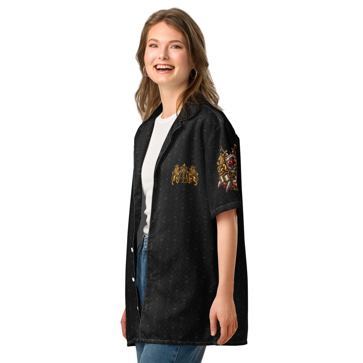 A woman modeling a black short-sleeve button-up shirt with gold and red heraldic crest embroidery on the chest and sleeve, worn over a white t-shirt and blue jeans against a plain white background.