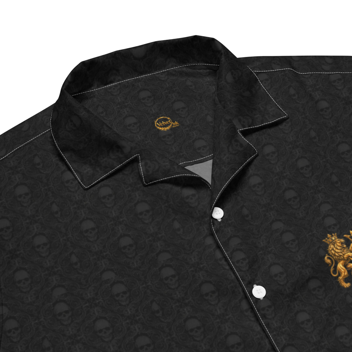 Close-up of a black button-up shirt with an all-over tonal skull pattern, white contrast stitching, and a gold embroidered lion crest on the chest.